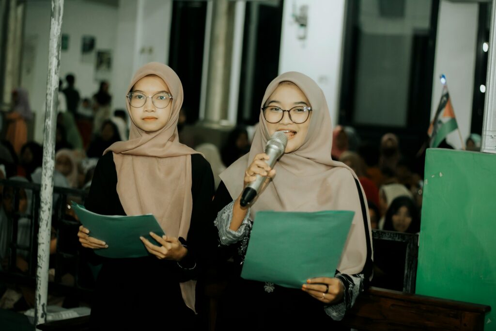 Two women in hijabs are holding microphones